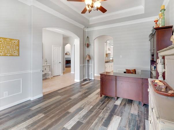 office area with ornamental molding, dark wood-type flooring, ceiling fan, and a tray ceiling