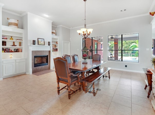 tiled dining room with a notable chandelier, a tile fireplace, built in shelves, and crown molding