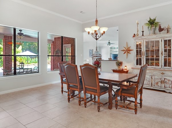 dining space featuring light tile patterned flooring, ceiling fan with notable chandelier, crown molding, and brick wall