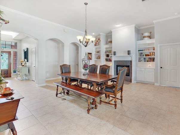 dining room featuring a chandelier, light tile patterned floors, a tiled fireplace, built in features, and ornamental molding