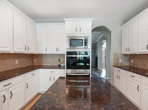 kitchen featuring appliances with stainless steel finishes, tasteful backsplash, dark stone counters, white cabinetry, and hardwood / wood-style flooring