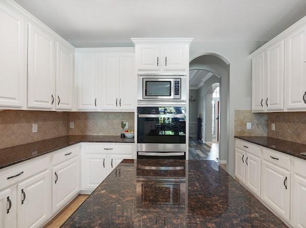 kitchen featuring appliances with stainless steel finishes, dark stone countertops, white cabinets, and backsplash