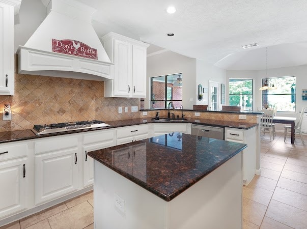 kitchen with dark stone countertops, gas cooktop, custom exhaust hood, a kitchen island, and sink