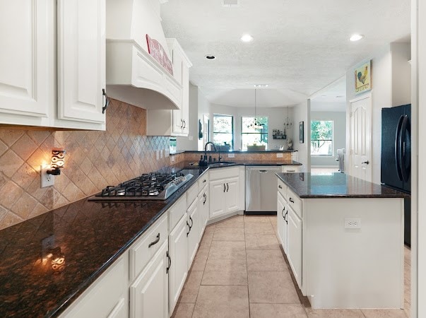 kitchen featuring kitchen peninsula, white cabinets, custom range hood, light tile patterned flooring, and stainless steel appliances