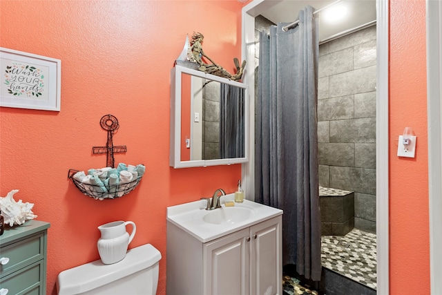 bathroom with toilet, a tile shower, and vanity