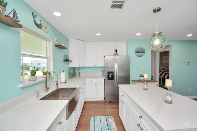 kitchen featuring sink, stainless steel refrigerator with ice dispenser, decorative light fixtures, light stone counters, and white cabinetry