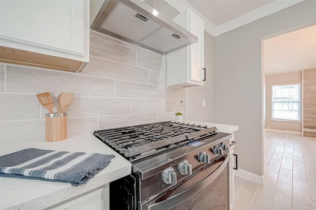 kitchen with wall chimney exhaust hood, white cabinetry, decorative backsplash, and stainless steel gas range