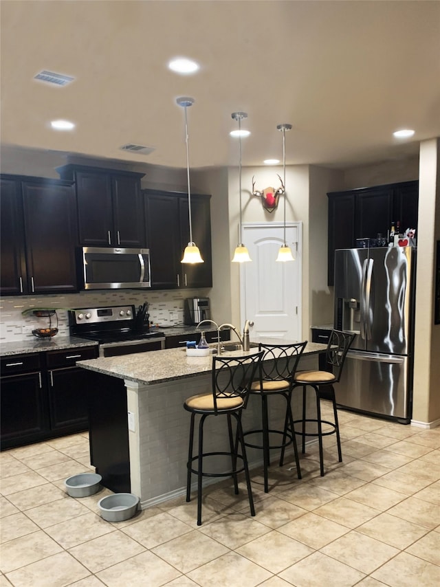 kitchen with stainless steel appliances, a kitchen breakfast bar, decorative backsplash, hanging light fixtures, and a center island with sink