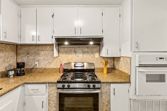 kitchen with stainless steel gas stove, oven, custom exhaust hood, white cabinets, and decorative backsplash