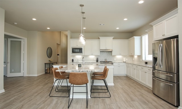 kitchen featuring tasteful backsplash, appliances with stainless steel finishes, an island with sink, and light hardwood / wood-style floors