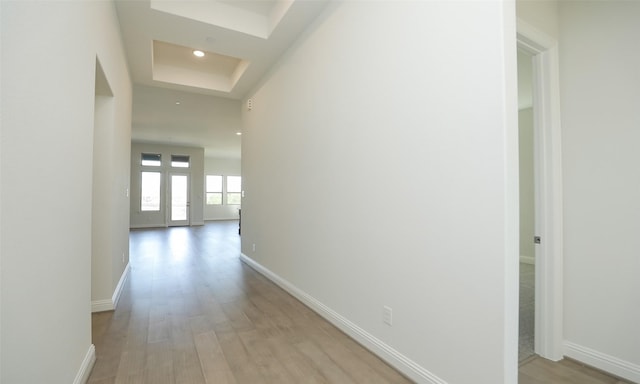 corridor with light wood-type flooring and a tray ceiling