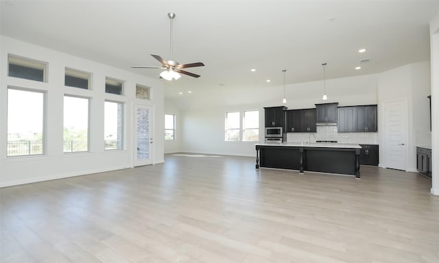 kitchen with a kitchen breakfast bar, backsplash, ceiling fan, a center island with sink, and light hardwood / wood-style floors