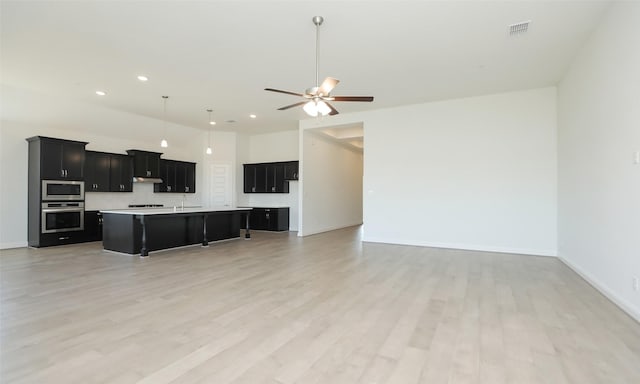 kitchen with appliances with stainless steel finishes, light wood-type flooring, a kitchen island with sink, and a kitchen breakfast bar