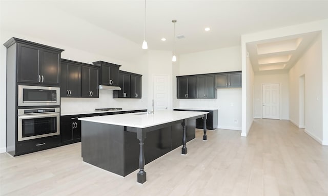 kitchen featuring appliances with stainless steel finishes, a kitchen breakfast bar, decorative light fixtures, light hardwood / wood-style floors, and an island with sink