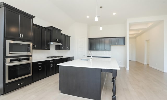 kitchen with hanging light fixtures, sink, light stone countertops, an island with sink, and appliances with stainless steel finishes