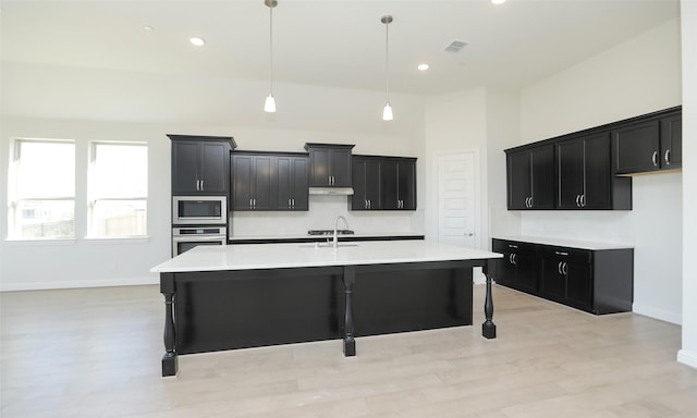 kitchen with a breakfast bar, stainless steel appliances, sink, pendant lighting, and an island with sink