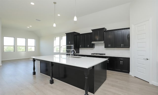 kitchen featuring appliances with stainless steel finishes, decorative light fixtures, a breakfast bar area, lofted ceiling, and an island with sink