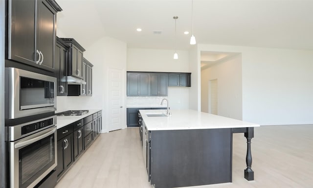 kitchen featuring a center island with sink, sink, appliances with stainless steel finishes, tasteful backsplash, and decorative light fixtures