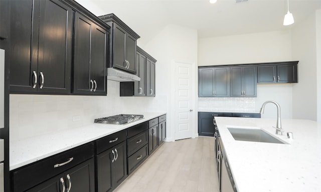 kitchen with sink, hanging light fixtures, light stone counters, backsplash, and stainless steel gas stovetop