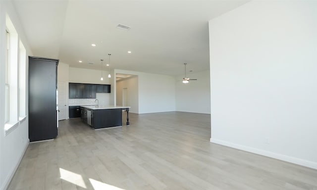 kitchen with ceiling fan, sink, tasteful backsplash, light hardwood / wood-style floors, and a center island with sink