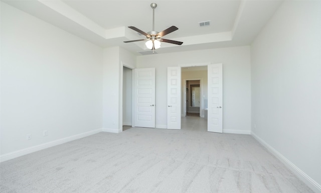 unfurnished bedroom featuring ceiling fan, light carpet, and a tray ceiling