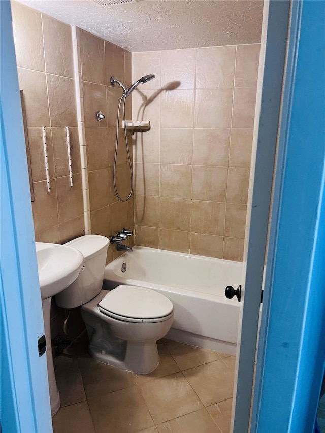 bathroom with a textured ceiling, toilet, tiled shower / bath combo, and tile patterned floors