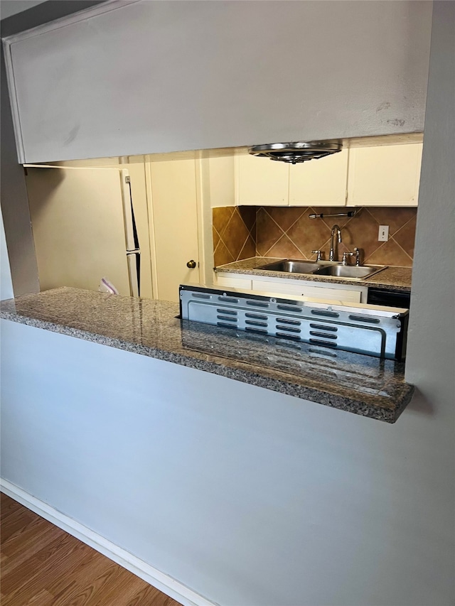 kitchen featuring dark stone countertops, white cabinets, wood-type flooring, backsplash, and sink