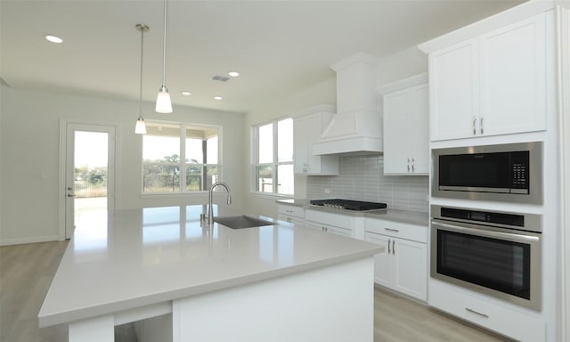 kitchen featuring sink, pendant lighting, a kitchen island with sink, custom range hood, and appliances with stainless steel finishes