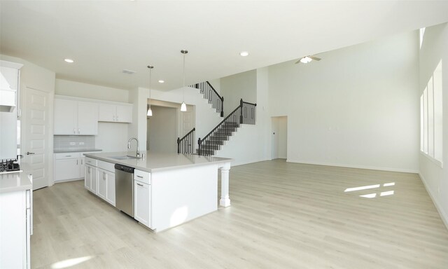 kitchen featuring white cabinetry, sink, hanging light fixtures, stainless steel dishwasher, and a kitchen island with sink