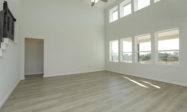 empty room featuring ceiling fan, light hardwood / wood-style floors, and a high ceiling