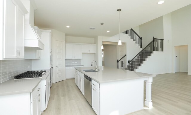 kitchen with custom exhaust hood, a center island with sink, hanging light fixtures, white cabinetry, and stainless steel appliances