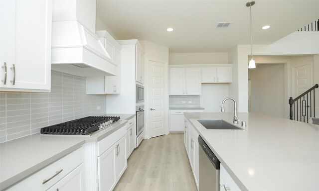 kitchen featuring backsplash, white cabinets, sink, hanging light fixtures, and appliances with stainless steel finishes