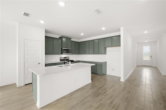 kitchen with light stone countertops, light hardwood / wood-style floors, a kitchen island with sink, stainless steel appliances, and sink