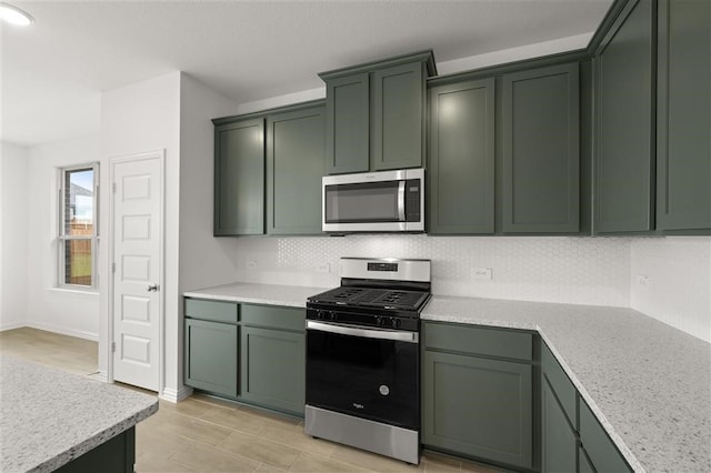 kitchen with green cabinetry, light stone countertops, stainless steel appliances, and tasteful backsplash