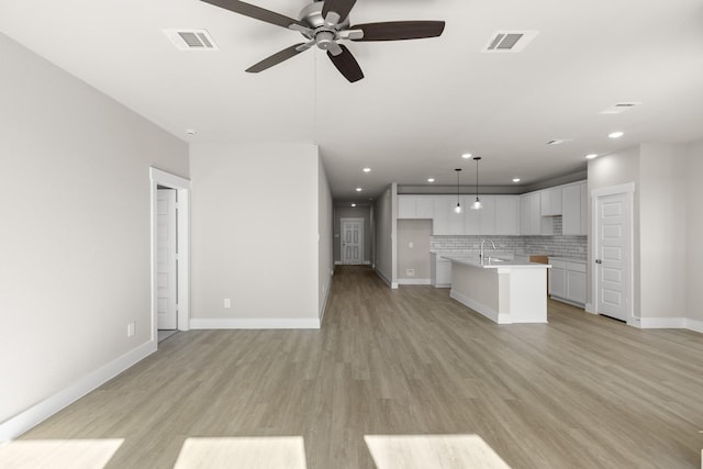 kitchen featuring decorative light fixtures, tasteful backsplash, white cabinetry, sink, and a kitchen island with sink