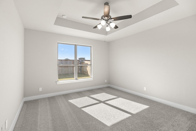 carpeted spare room featuring a tray ceiling and ceiling fan