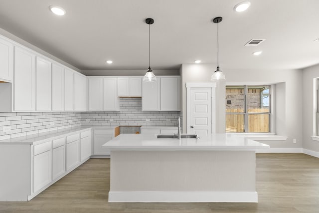 kitchen featuring sink, white cabinetry, decorative light fixtures, a center island with sink, and light hardwood / wood-style flooring