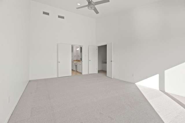 unfurnished bedroom featuring a towering ceiling, ensuite bath, light carpet, and ceiling fan