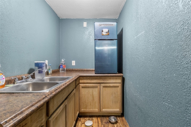 kitchen featuring a textured wall, a sink, and wood finished floors