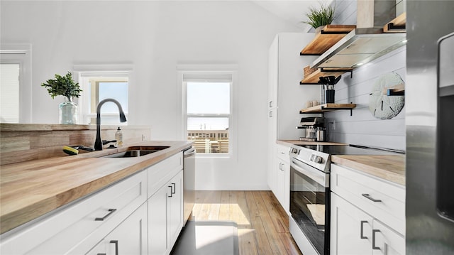 kitchen with open shelves, wall chimney range hood, white cabinetry, and stainless steel appliances