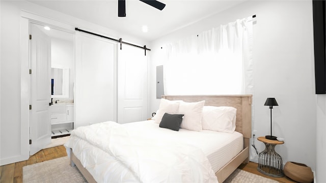 bedroom with ceiling fan, light hardwood / wood-style flooring, ensuite bath, and a barn door