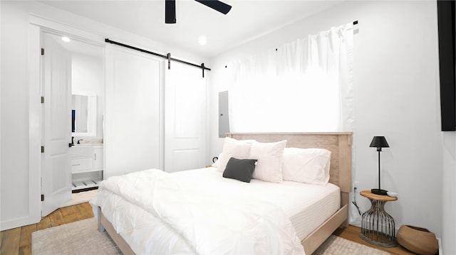 bedroom featuring light wood-type flooring, a barn door, a ceiling fan, and ensuite bathroom