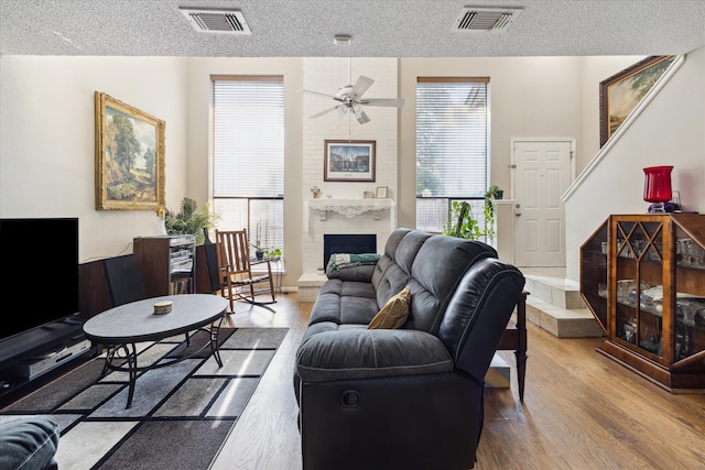 living room featuring ceiling fan, a fireplace, a textured ceiling, and light hardwood / wood-style floors