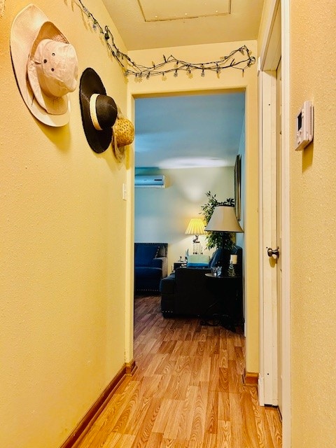 corridor with light wood-type flooring and a wall unit AC