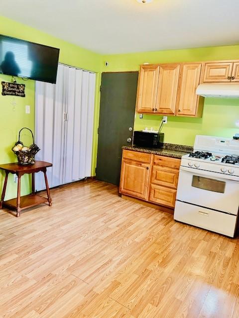 30470 Reids Prairie Rd, Waller, TX 77484 - kitchen with white gas stove, under cabinet range hood, light wood finished floors, and black microwave