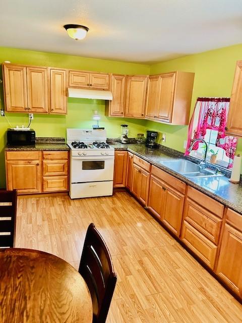 30470 Reids Prairie Rd, Waller, TX 77484 - kitchen featuring white range with gas stovetop, under cabinet range hood, black microwave, a sink, and dark countertops
