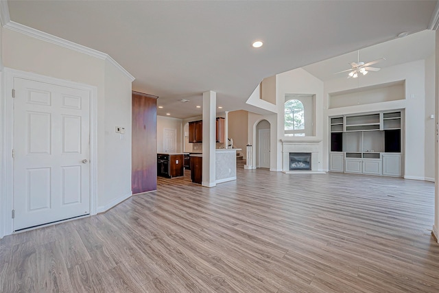 unfurnished living room with a fireplace, built in features, ornamental molding, ceiling fan, and light hardwood / wood-style flooring