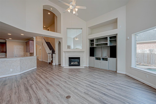 unfurnished living room with built in shelves, stairway, light wood-type flooring, a fireplace, and high vaulted ceiling