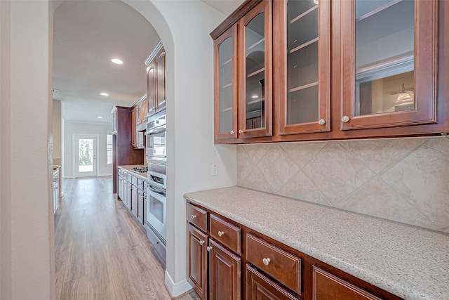 kitchen with light hardwood / wood-style flooring, crown molding, oven, and tasteful backsplash