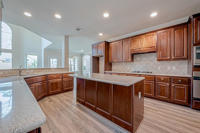 kitchen featuring tasteful backsplash, a kitchen island, sink, crown molding, and light wood-type flooring